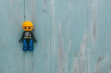 Sarı kasklı ve mavi çizmeli gülümseyen lego işçisi. Kopya alanı mavi ahşap arka planda.