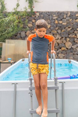 Düşünceli çocuk havuzdan çıkıyor, bir sonraki hamlesini düşünüyor boş bir anda, yeşil bir bahçeyle çevrili..