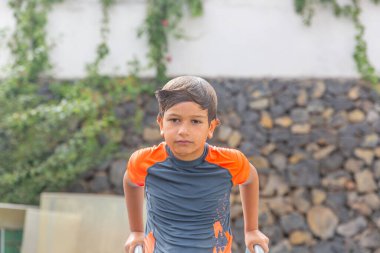 Dalgın genç bir çocuk yüzme sonrası hareketsiz durur, ıslak saçı geriye doğru kayar, yemyeşil bir arka planda, sessizce havuzda geçirdiği zamanı yansıtır.