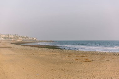 Plaj, arkasında berrak mavi bir okyanus olan güzel, boş bir kum parçasıdır. Gökyüzü açık ve güneş parlıyor. Huzurlu ve huzurlu bir atmosfer yaratıyor.