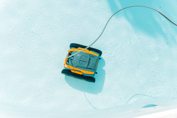 Роботизированное устройство плавает в бассейне. Устройство жёлтое и чёрное. Бассейн голубой в летний сезон