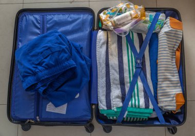 Bir bavul açık ve içinde mavi bir gömlek, çizgili bir havlu ve bir çift mavi şort var.