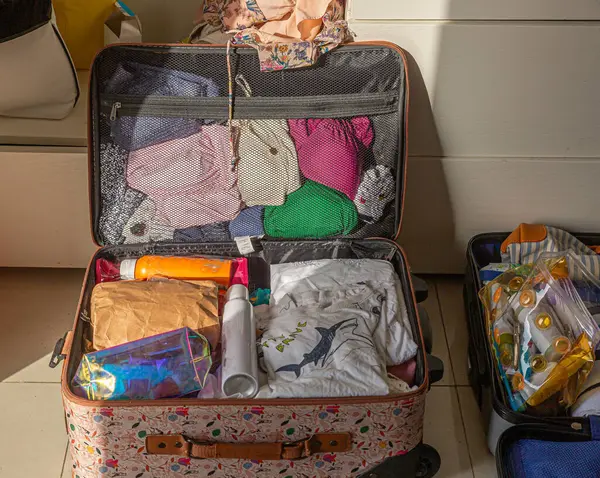 Bir bavul açık ve giysilerle dolu. Bavulda birkaç şişe ve bir fincan var.