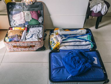 Bir bavul açık ve içinde giysiler var. Çanta mavi ve sapı var. Arka planda bir sandalye var.