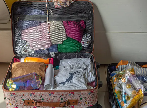 Bir bavul giysi ve tuvalet eşyalarıyla dolu. Bavul bir katta. Yerde iki bavul var.