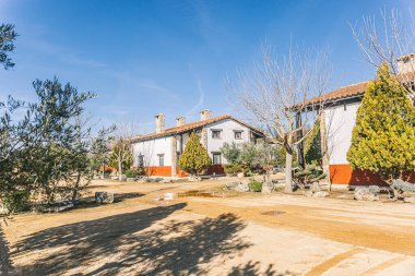 Kırmızı tuğladan duvarı ve beyaz çatısı olan bir ev. Evin etrafı ağaçlarla çevrili ve garaj yolu var.