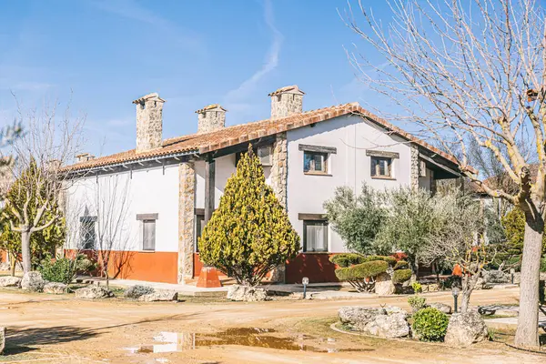 Kırmızı tuğladan duvarı ve beyaz çatısı olan bir ev. Ev ağaçlarla çevrili ve güneşli bir günde garaj yolu var.