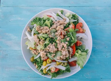 Marullu, domatesli ve zeytinli bir salata beyaz bir kasede servis edilir. Kase mavi bir masanın üzerine konur. İki kaşık klozete konur, kullanılmaya hazır.