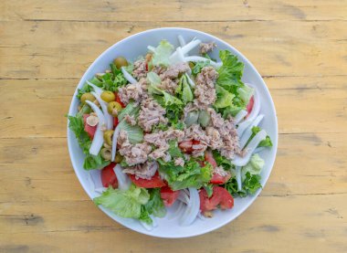 Bir çeşit sebzeli salata ve birkaç parça et. Salata, sarı ahşap bir masada beyaz bir kasede servis edilir.