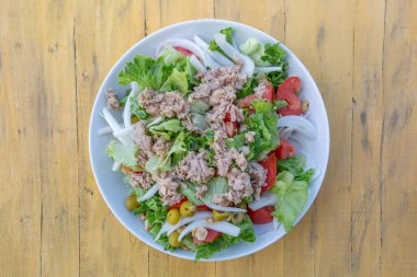 Bir çeşit sebzeli salata ve birkaç parça et. Salata ahşap bir masada beyaz bir kasede servis edilir.