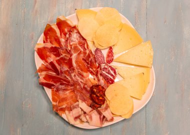 Jambon, peynir ve kraker ile bir tabak yemek. Tabak beyaz ve yemek dairesel bir şekilde düzenlenmiş.