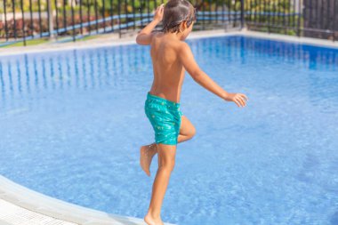 Bir çocuk havuzda oynuyor. Havuz bir çitle çevrili. Çocuk yeşil bir mayo giyiyor..