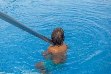 Suda mavi mayo giyen bir çocuk var. O kameraya bakıyor.