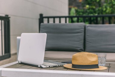 Hasır şapka ve bardağın yanındaki masada bir dizüstü bilgisayar açık. Sahne, sakin ve sakin bir atmosferi işaret ediyor.