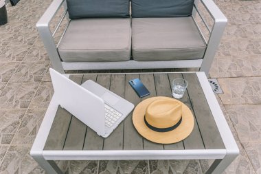 Bir dizüstü bilgisayar, bir cep telefonu ve bir hasır şapka ahşap bir masada duruyor.