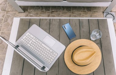 Bir dizüstü bilgisayar ve bir şapka ahşap bir masada. Laptop açık ve şapka onun üzerine yerleştirilmiş. Sahne, rahat ve rahat bir atmosferi işaret ediyor.