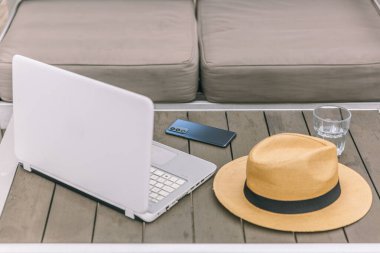 Bir dizüstü bilgisayar, cep telefonu ve şapka ahşap bir masada. Laptop açık ve cep telefonu da yanında.