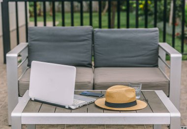 Bir dizüstü bilgisayar ve bir şapka bir kanepenin yanındaki masada. Sahne, rahatlamış ve sakin bir atmosferi işaret ediyor. Muhtemelen birinin işe ara verdiğini ya da ders çalıştığını gösteriyor.