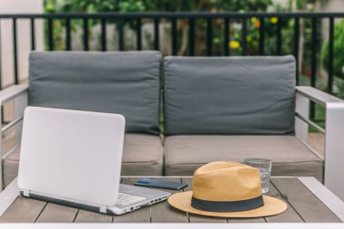 Bir dizüstü bilgisayar ve bir şapka ahşap bir masada. Laptop açık ve şapka masanın üzerine yerleştirildi. Sahne, sakin ve sakin bir atmosferi işaret ediyor.