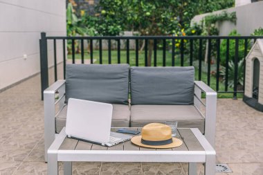 Bir dizüstü bilgisayar bir masanın üzerinde bir şapkanın yanında. Şapka dışarıdaki ahşap masada.