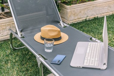 Bir dizüstü bilgisayar ve bir şapka katlanır sandalyede. Dizüstü bilgisayar açık ve şapkası üstünde. Sahne, sakin ve sakin bir atmosferi işaret ediyor.