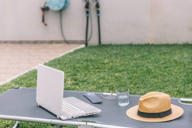 Bir dizüstü bilgisayar ve bir şapka katlanır sandalyede. Sahne, sakin ve sakin bir atmosferi işaret ediyor.