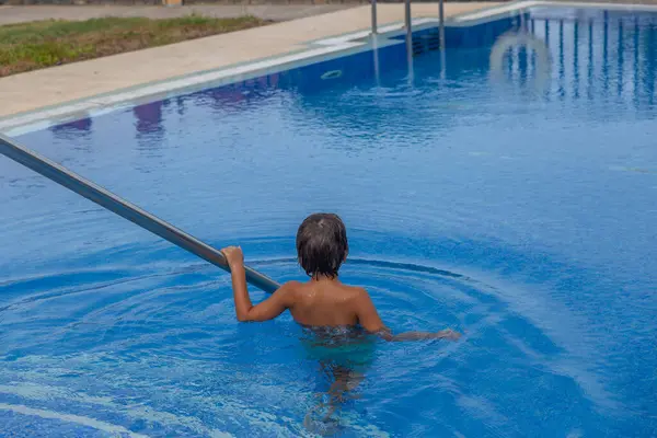 Bir çocuk havuzda elinde erişteyle bekliyor. Havuz mavi ve su sakin.