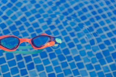 Bir çift gözlük havuzda yüzüyor. Gözlükler turuncu ve mavi. Havuz mavi ve su sakin.