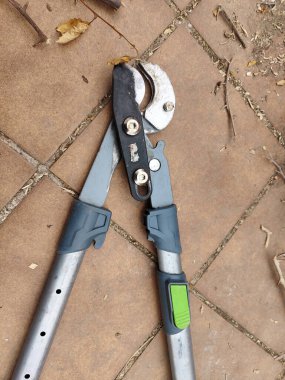 Yeşil saplı bir budama makası fayanslı bir zeminde oturur. Makas açık ve kullanıma hazır.