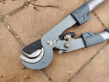 Siyah bıçaklı ve gri saplı bir budama makası. Makaslar fayanslı bir yüzeyde duruyor.