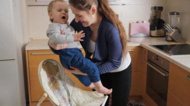 Küçük bebek ağlarken ve çığlık atarken annesi onu mutfakta şezlongda oturtuyor. Ebeveynlik kavramı, sağlıklı beslenme ve bebek bakımı