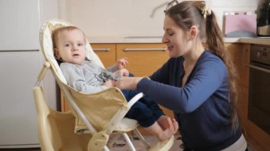 Young mother fastening seat belts on baby feeding highchair before giving food to her son. Concept of parenting, healthy nutrition and baby care.