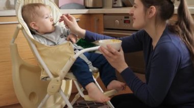 Little baby being silly and naughty while eating porridge in highchair. Concept of parenting, healthy nutrition and baby feeding