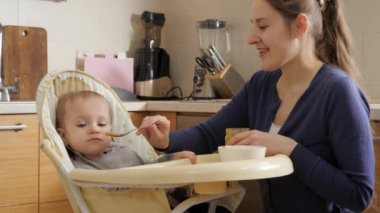 Portrait of smiling mother feeding her baby son with porridge from spoon. Concept of parenting, healthy nutrition and baby care