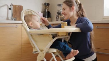 Küçük bebek mutfakta şezlongda oturup meyveli lapa yiyor. Ebeveynlik kavramı, sağlıklı beslenme ve bebek bakımı