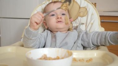 Cute baby boy sitting in highchair playing with food and making mess. Concept of parenting, healthy nutrition and baby feeding