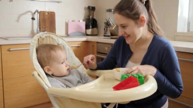 Adorable baby sitting in highchair eating and smiling at his mother. Concept of parenting, healthy nutrition and baby feeding