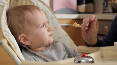 Closeup portrait of little baby boy having breakfast in highchair at home. Concept of parenting, healthy nutrition and baby feeding.