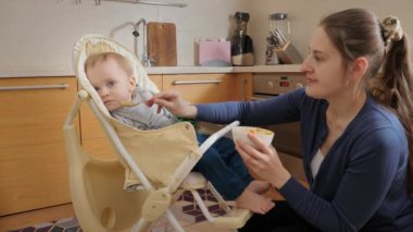 Little baby refusing eating in highchair and turning his head away from spoon. Concept of parenting, healthy nutrition and baby feeding