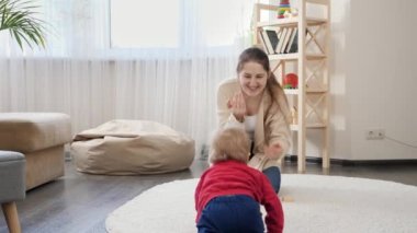 Sevimli bir erkek bebek yerde annesine doğru sürünüyor ve top atıyor. Bebek gelişimi, aile oyunları, ilk adımlar, ebeveynlik ve bakım