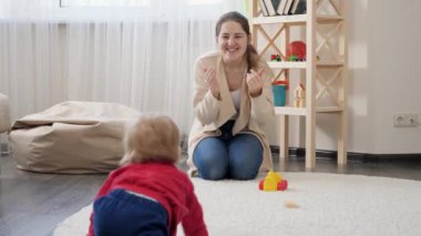 Mutlu gülen çocuk yerde sürünüyor ve genç annesiyle top oynuyor. Bebek gelişimi, aile oyunları, ilk adımlar, ebeveynlik ve bakım.