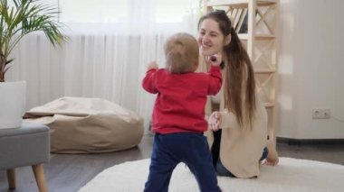 Tatlı bebek yürümeyi öğreniyor ve annesinin halıda oturması için adımlar atıyor. Bebek gelişimi, aile oyunları, ilk adımlar, ebeveynlik ve bakım.