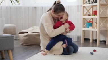 Gülümseyen mutlu bir anne bebeğine sarılıyor ve onu gıdıklıyor. Bebek gelişimi, aile oyunları, birlikte eğlenmek, ebeveynlik ve bakım..