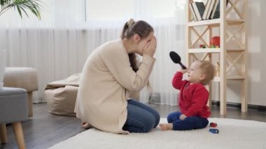 Gülümseyen mutlu anne yerde oturup küçük oğluyla oynuyor. Bebek gelişimi, aile oyunları, birlikte eğlenmek, ebeveynlik ve bakım..