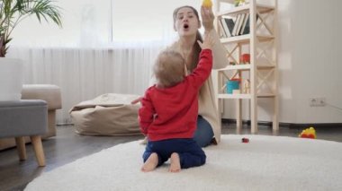 Genç bir anne, küçük oğluna oyuncaklar vererek ayakta durup yürümeyi öğretiyor. Bebek gelişimi, aile oyunları, ilk adımlar, ebeveynlik ve bakım.