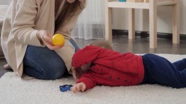 Mutlu, gülümseyen bir kadın. Küçük oğlunu kucaklıyor ve yerde yatıyor. Bebek gelişimi, aile oyunları, ilk adımlar, ebeveynlik ve bakım.