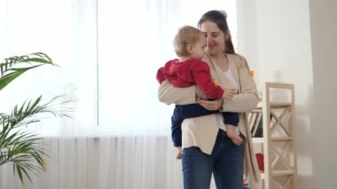 Güzel bir anne bebeğini kucağına alıp oturma odasında ona oyuncaklar gösteriyor. Bebek gelişimi, aile oyunları, ilk adımlar, ebeveynlik ve bakım.