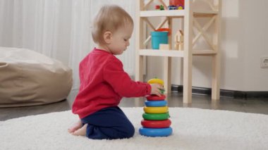 Küçük bebek oturma odasında renkli oyuncak piramidiyle oynuyor. Bebek gelişimi, aile oyunları, ilk adımlar, ebeveynlik ve bakım.