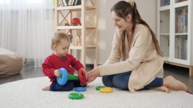 Güzel, genç bir anne, küçük oğluyla yerde oynuyor ve oyuncak kulesi kuruyor. Bebek gelişimi, çocuk oyunları, eğitim ve öğrenim