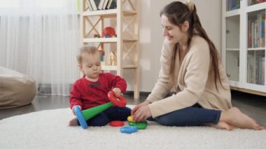 Genç bir kadın renkli yüzüklerle oyuncak kulesi yapmasına yardım ediyor. Bebek gelişimi, çocuk oyunları, eğitim ve öğrenim